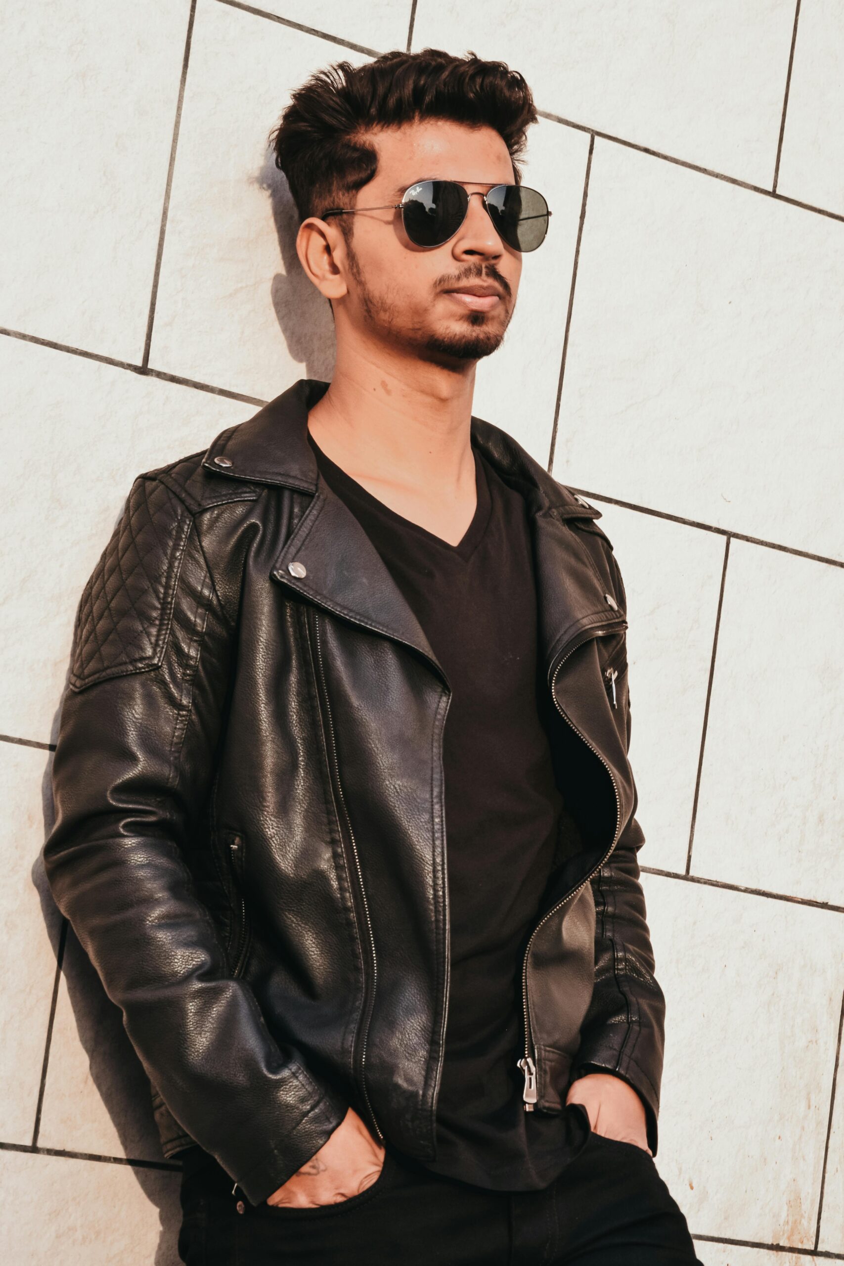 pexels photo 1124468 1124468 Fashionable young man in sunglasses and leather jacket posing against a tiled wall outdoors.