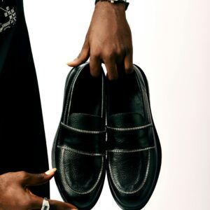 A person holding elegant black leather dress shoes with fashion accessories.