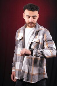 Casual man in checkered shirt looks at watch on red background, concept of punctuality. for look check stylish shirts for men